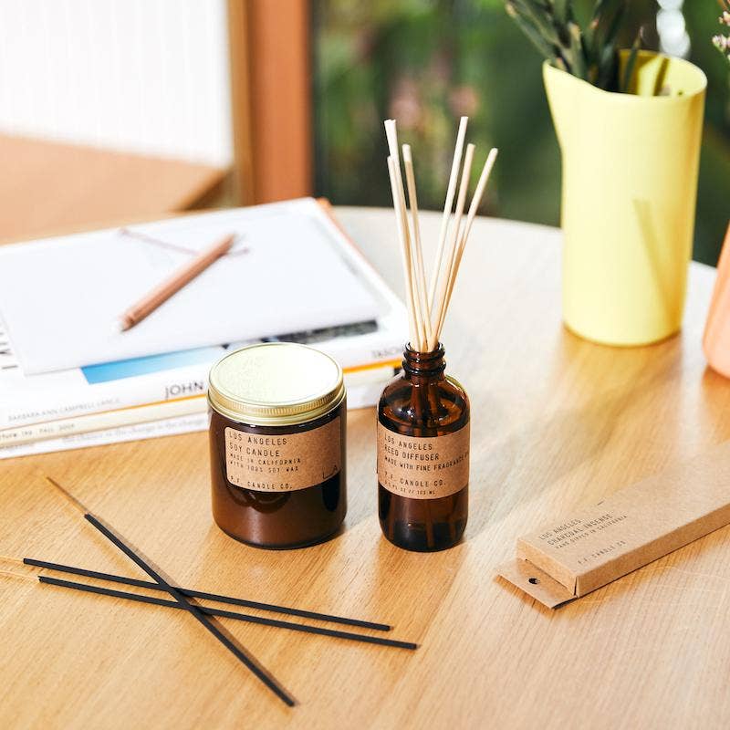 Los Angeles soy candle with matching reed diffuser and incense on a wood table near books