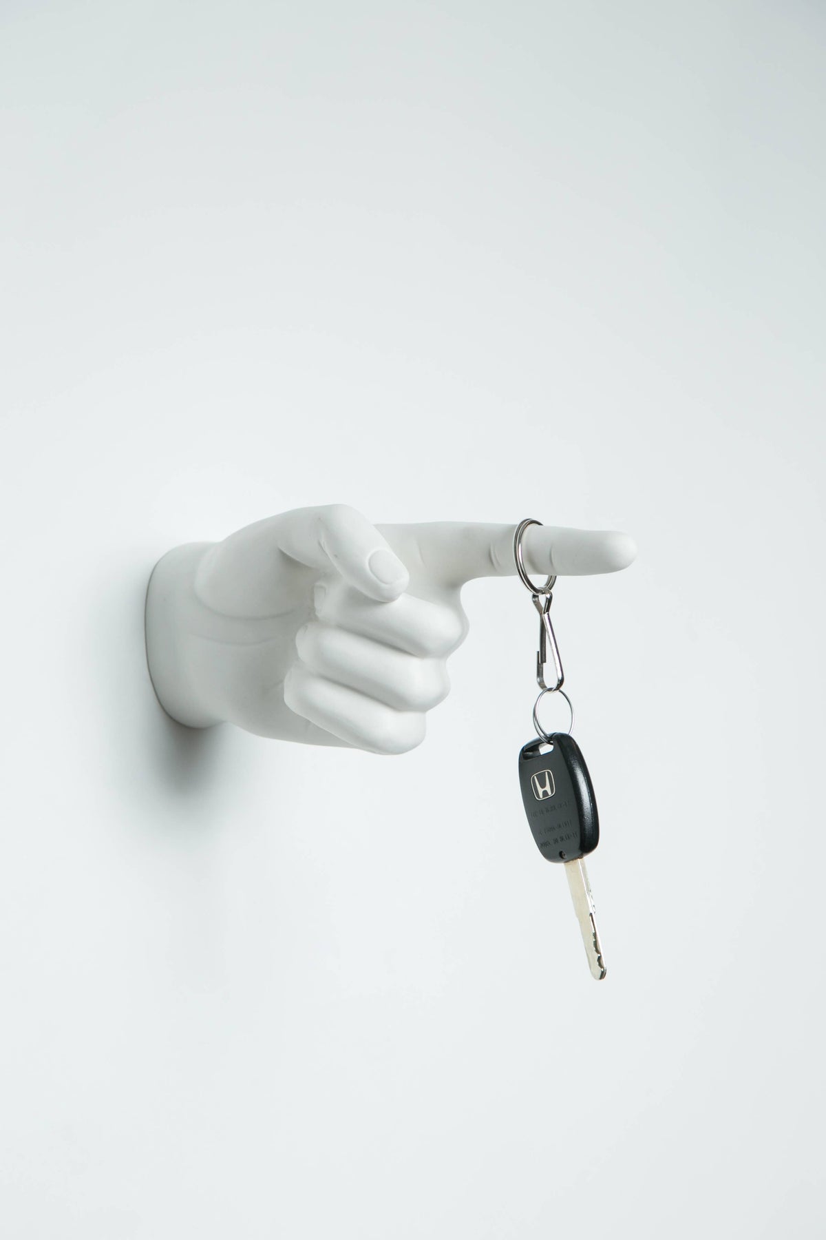 White pointing hand wall hook with a car key on a clip hanging from the extended finger
