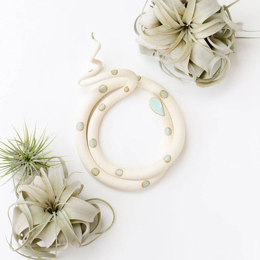 Coiled cream ceramic snake with mint green spots and a raised tail, shown from above with air plants