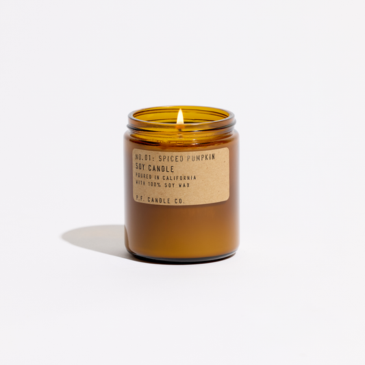 Lit Spiced Pumpkin soy candle in an amber jar without its lid, flame visible