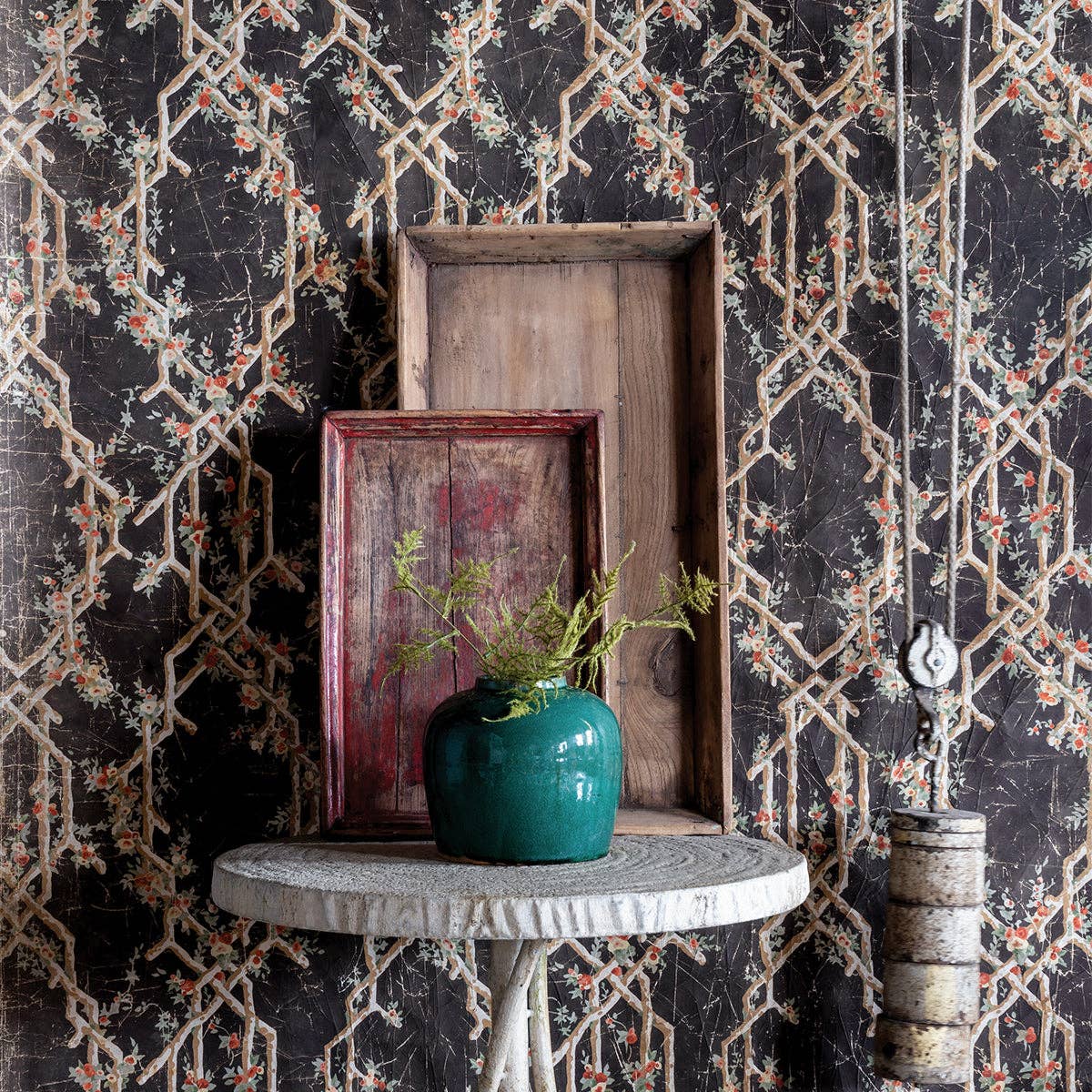 Green Dynasty ginger jar with fern sprigs on a round side table before wood trays and patterned wallpaper