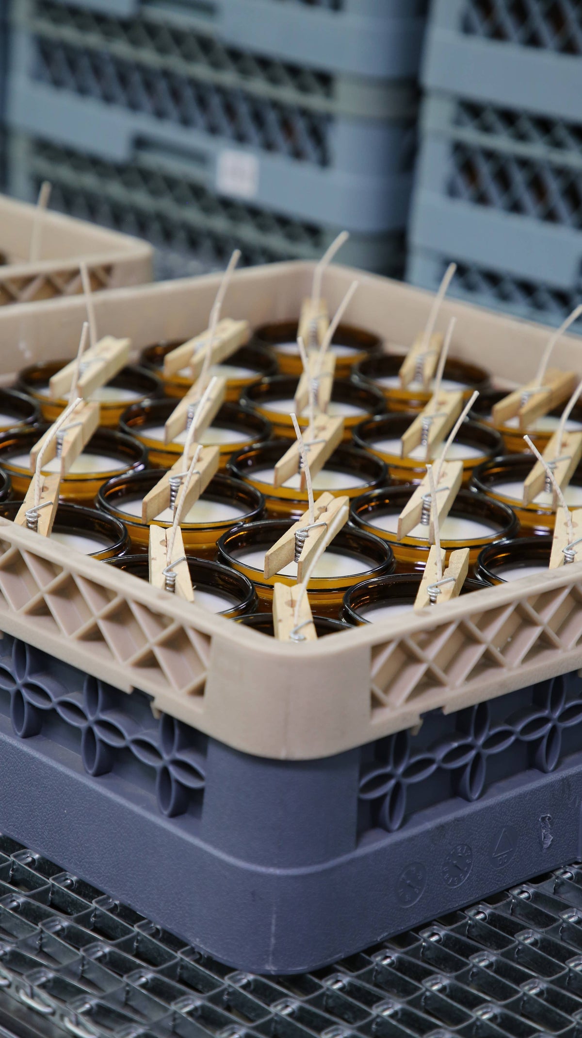 Amber candle jars with wicks held by wooden clothespins in a crate while the wax sets
