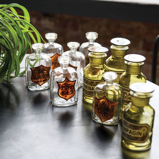 Clear apothecary bottles with copper shield labels styled with olive glass bottles on a dark table