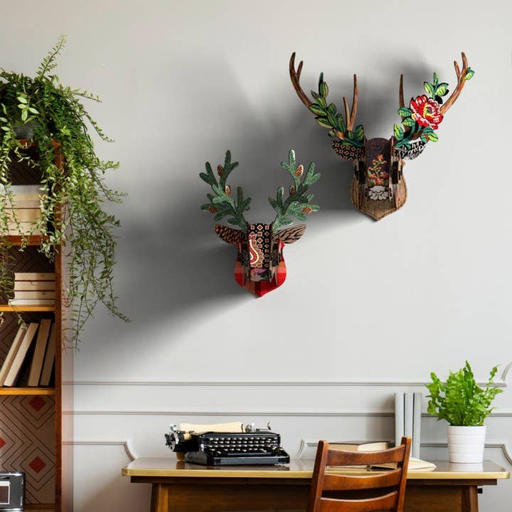 Floral deer head with a red rose beside a smaller red patterned deer head, on a wall above a desk and typewriter