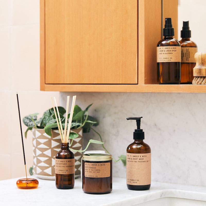Amber & Moss incense in an amber glass holder next to a matching diffuser, jar candle, and hand soap