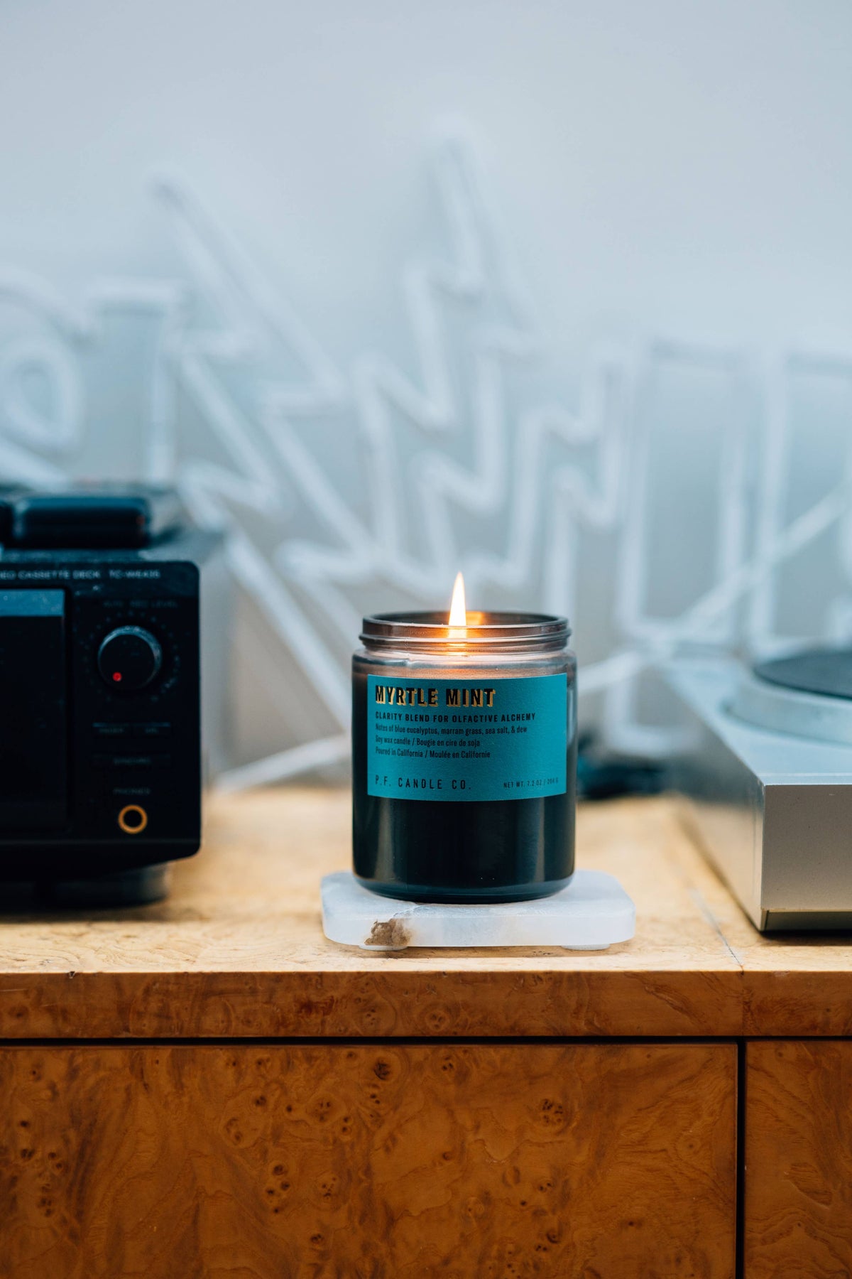 Lit Myrtle Mint candle on a white stone coaster on a burl wood cabinet beside a tape deck
