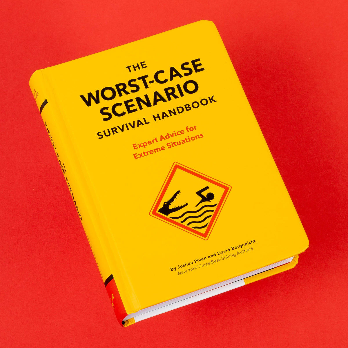Yellow Worst-Case Scenario Survival Handbook lying at an angle on a bright red background