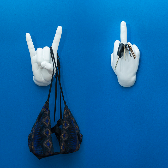 Rock On hand hook holding a bra on a blue wall next to a middle-finger hand hook with keys