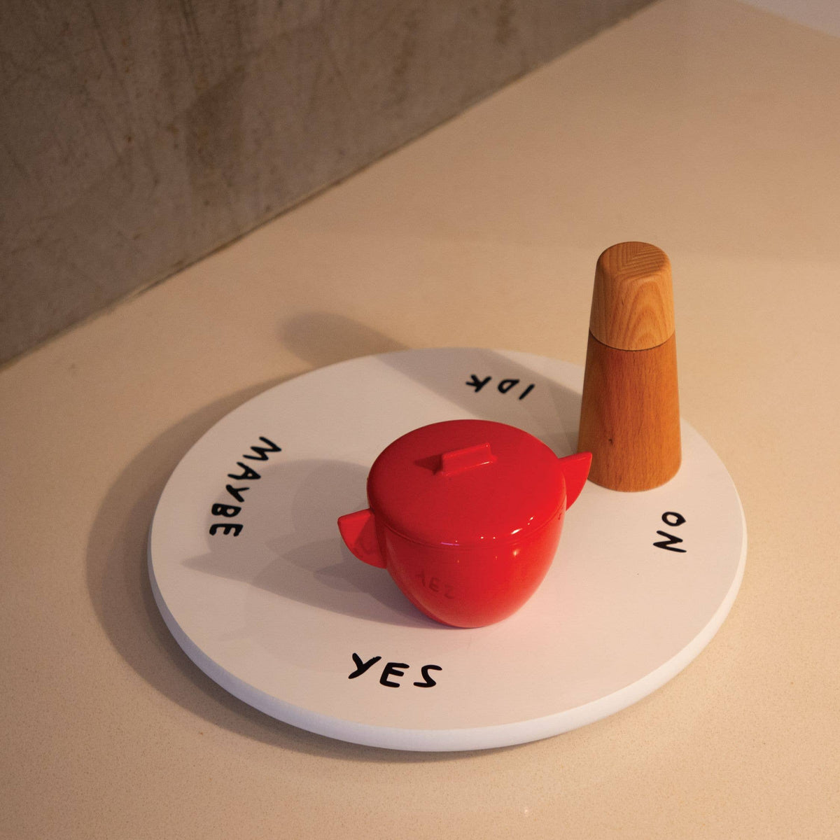 Indecisive Lazy Susan holding a red lidded pot and a wooden pepper mill on a beige countertop