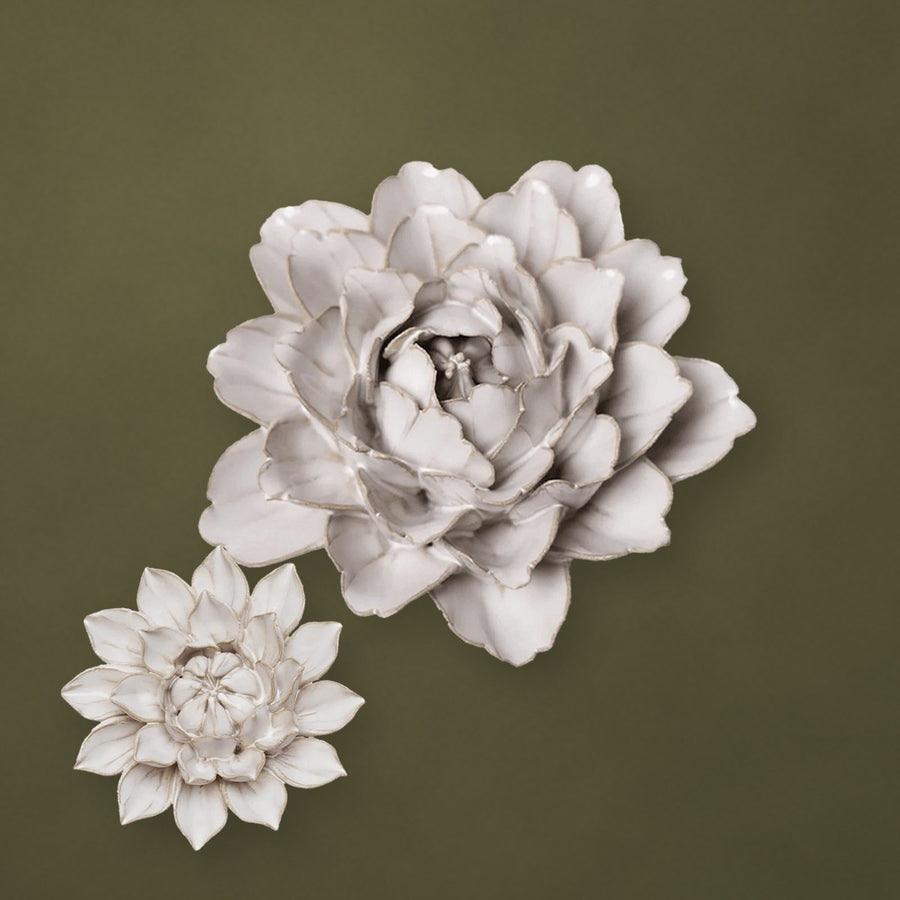 Ivory ceramic peony and a small aster on an olive-green plaster wall