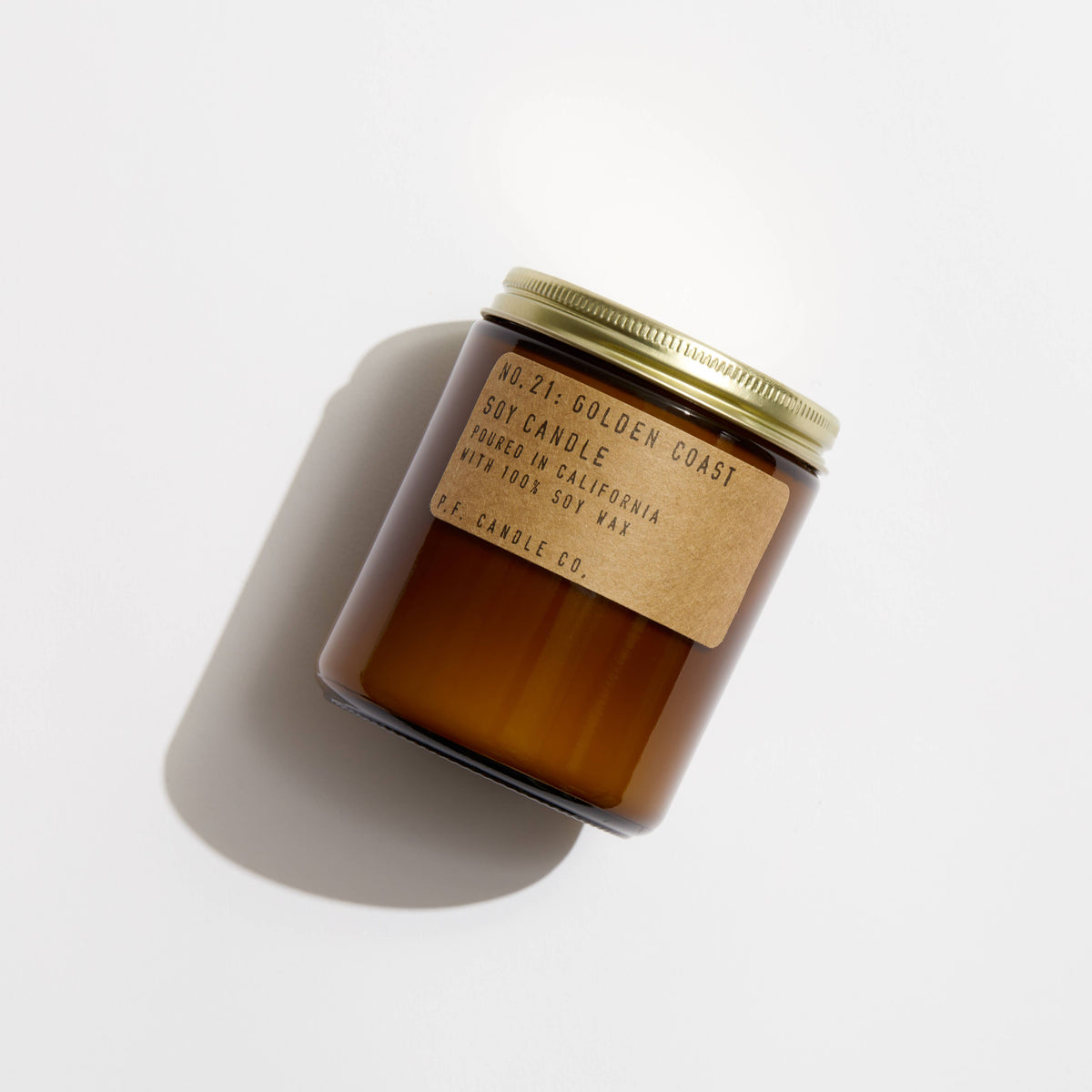 Golden Coast amber jar candle tilted on white, kraft label reading No. 21 Golden Coast soy candle