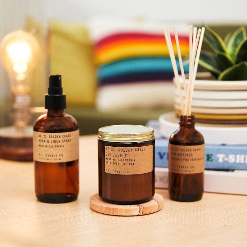 Golden Coast soy candle with matching room spray and reed diffuser on a table in a cozy room