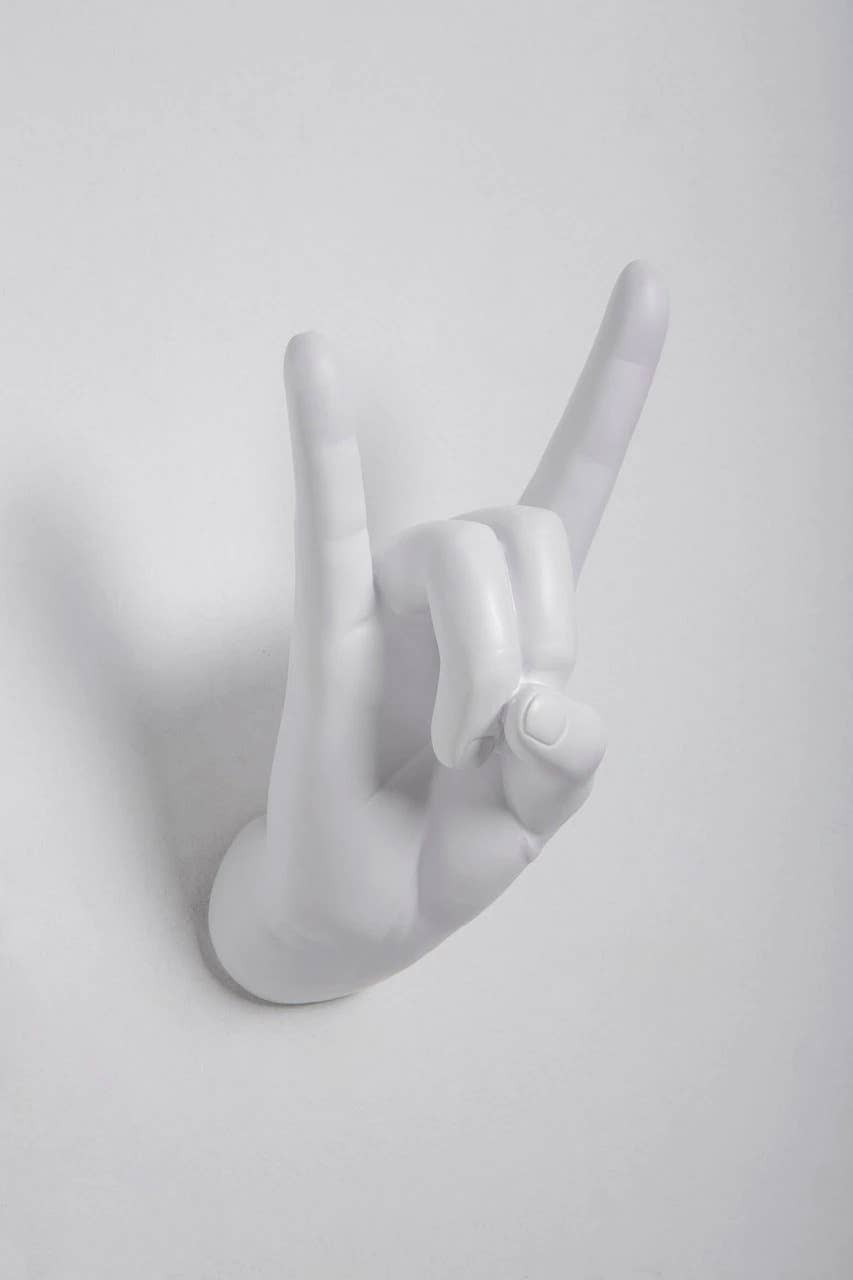 White Rock On hand wall hook making the horns gesture, shown at an angle on a white wall