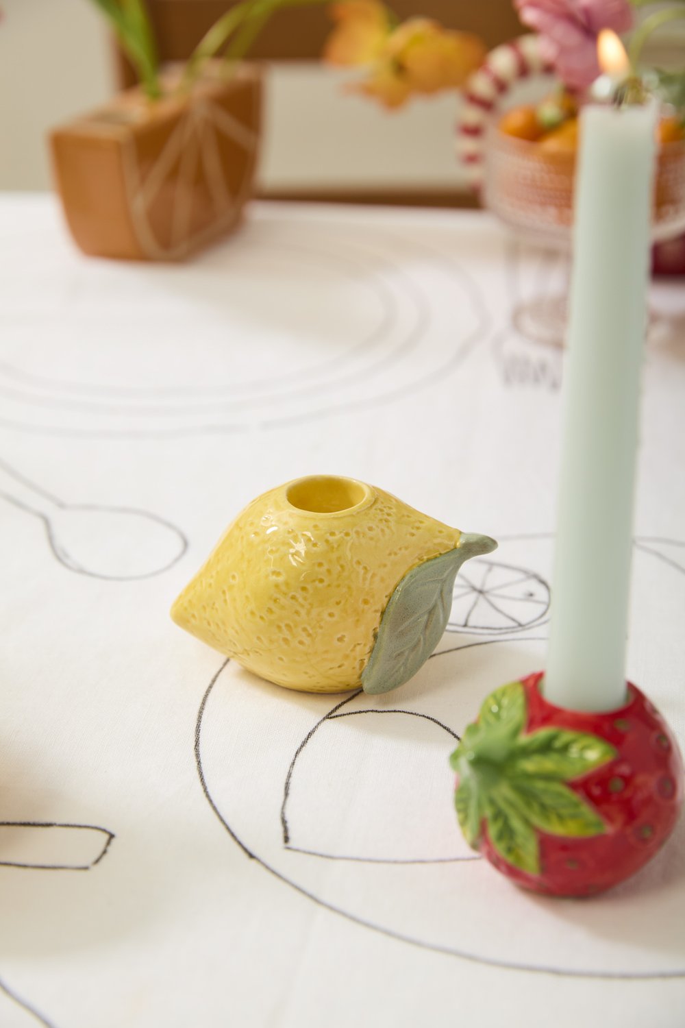 Lemon candleholder on a dining table next to a strawberry candleholder holding a mint green taper