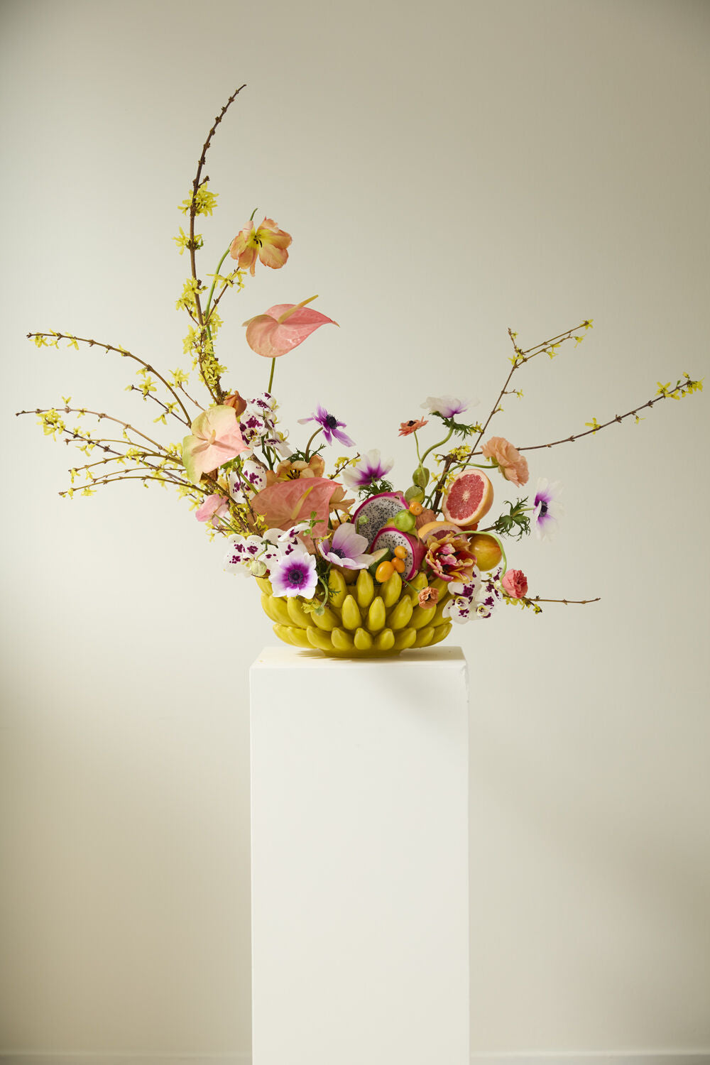 Banana bowl on a white pedestal holding a tall arrangement of flowers, branches and sliced fruit