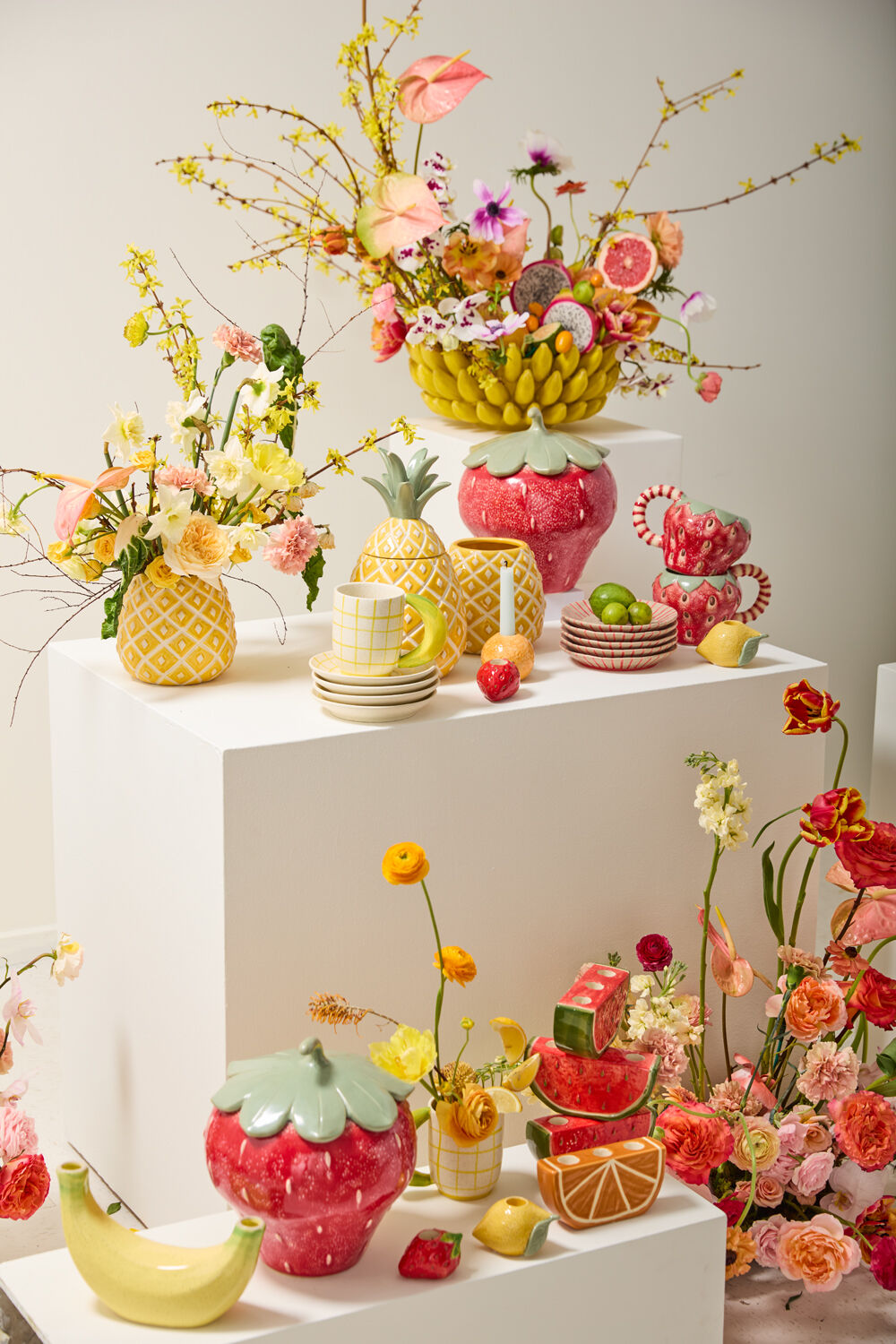 Banana bowl with a floral arrangement atop pedestals among strawberry, pineapple and fruit ceramics