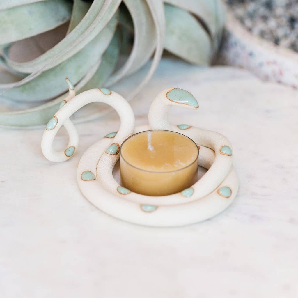 Cream ceramic snake tealight holder with turquoise spots coiled around a beeswax tealight, air plant behind