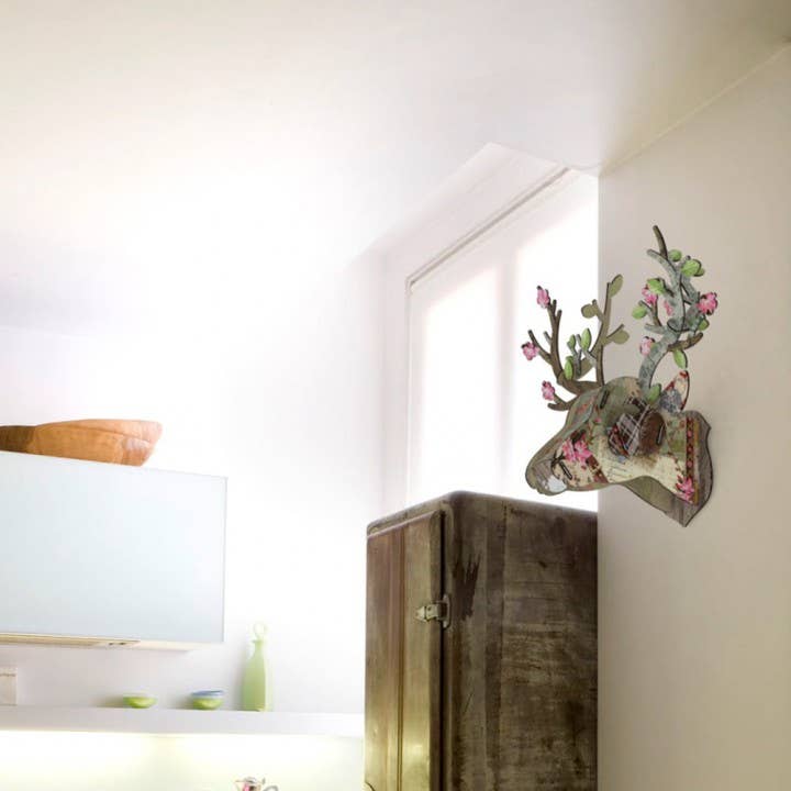 Eco deer head mounted on a white wall above a rustic wooden cabinet in a bright room