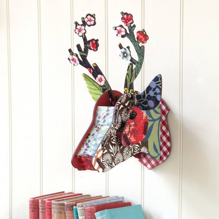 Flower Blow-Up deer head hung on a white paneled wall above a row of books