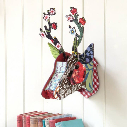 Flower Blow-Up deer head hung on a white paneled wall above a row of books