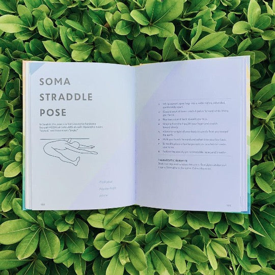 High Yoga book open to the Soma Straddle Pose page, laid on a bed of green leaves