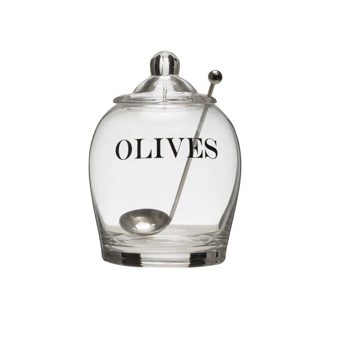 Clear glass olive jar with OLIVES in black lettering, knobbed glass lid and a steel spoon through the lid