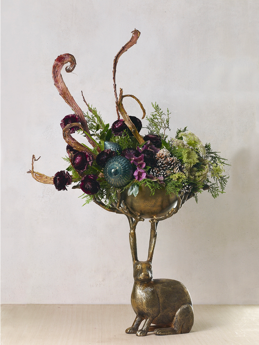 Eric branch bowl holding a tall arrangement of burgundy ranunculus, greenery, pinecones and a teal ornament