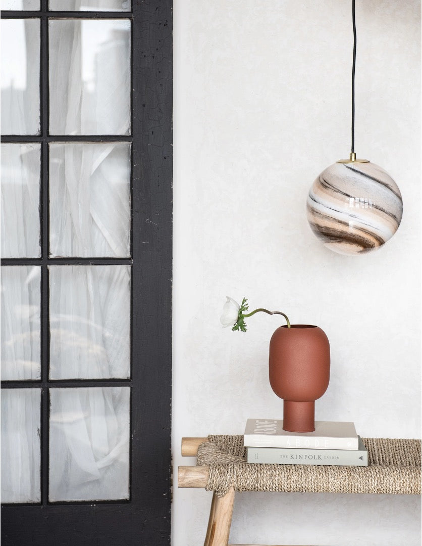 Textured metal vase, matte Sienna color, round on stack of books with single flower stem. 