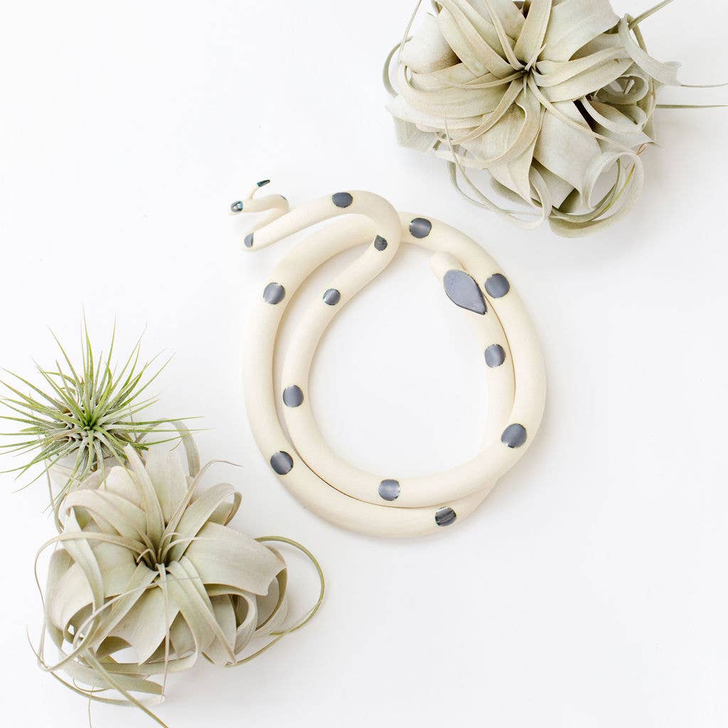 Coiled cream ceramic snake with dark gray spots, shown from above between air plants