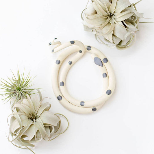 Coiled cream ceramic snake with dark gray spots, shown from above between air plants