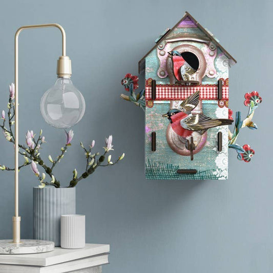 Playmates bird house mounted on a blue wall beside a brass lamp and a vase of magnolia branches
