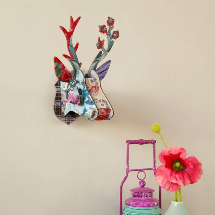 Eco deer head hung on a cream wall above a pink lantern and a red poppy in a vase