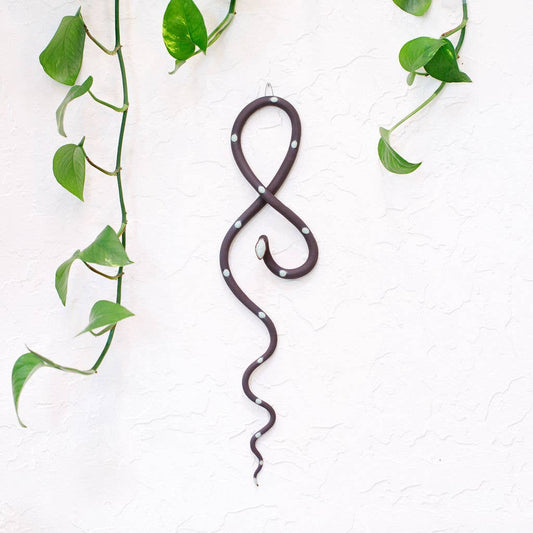 Ceramic wall snake in dark brown with white dots, hung in a figure-eight loop beside pothos vines